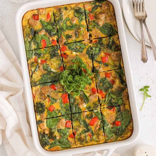 Vegetable and sausage egg bake, cut into 12 pieces, in a 9x13 baking dish with plates and 2 forks on the side.