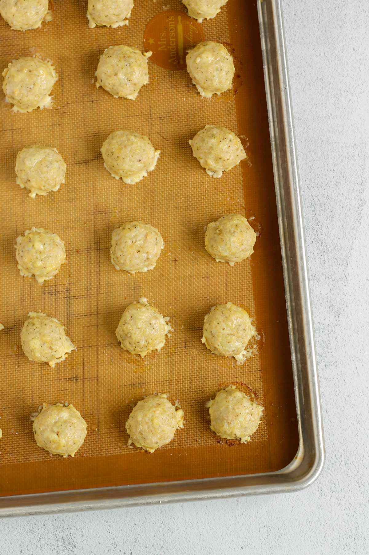 Cooked chicken meatballs on a silicone mat lined baking sheet.