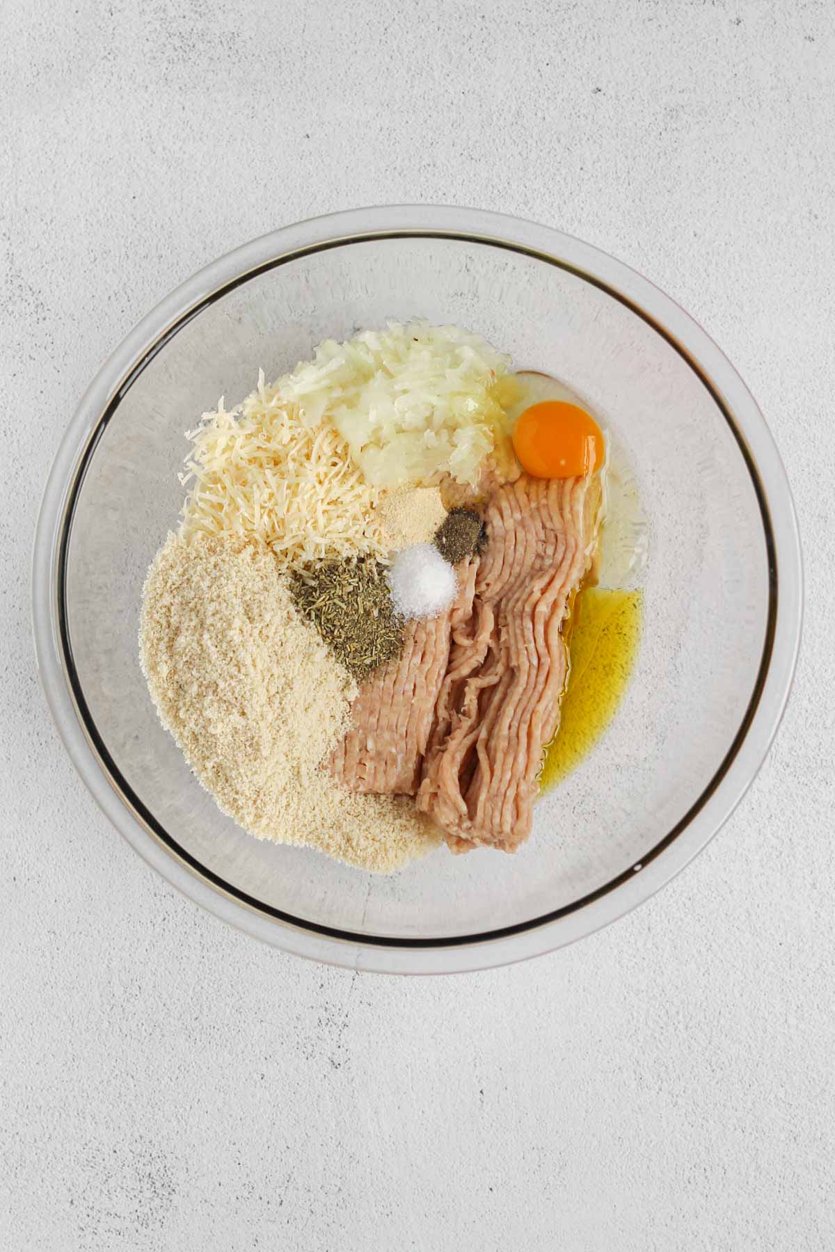 Ingredients needed for gluten-free chicken meatballs in a glass mixing bowl unmixed.