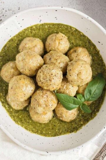 Chicken meatballs stacked in a bowl with pesto with a small bowl of pesto on the side.
