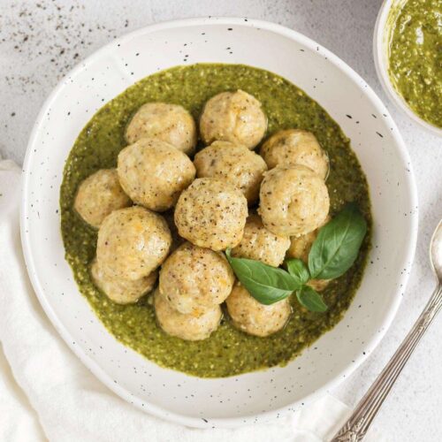 Chicken meatballs stacked in a bowl with pesto with a small bowl of pesto on the side.