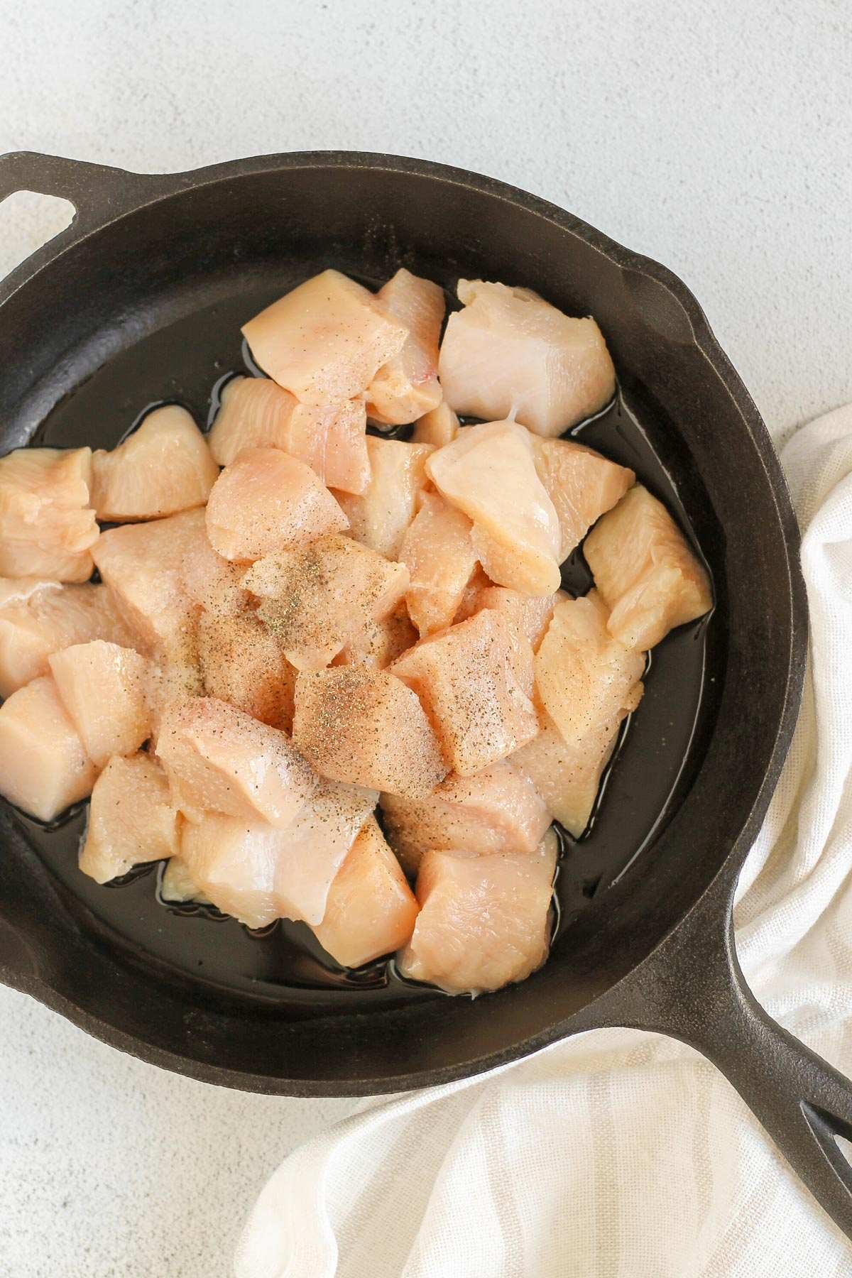 Raw diced chicken sprinkled with salt and pepper in a cast iron skillet.