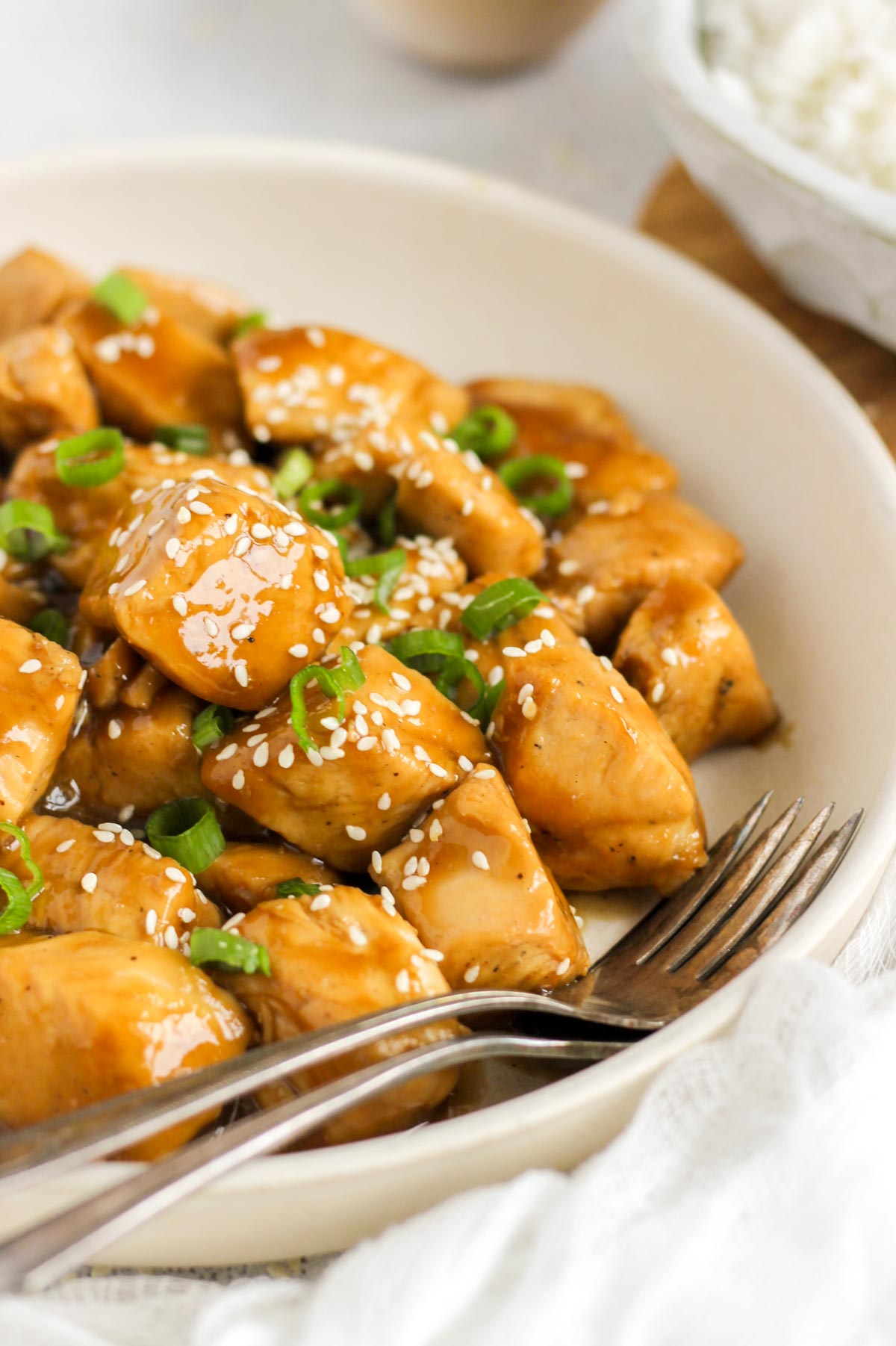 Teriyaki chicken pieces topped with sliced green onions and sesame seeds in a serving bowl with two forks in the bowl.