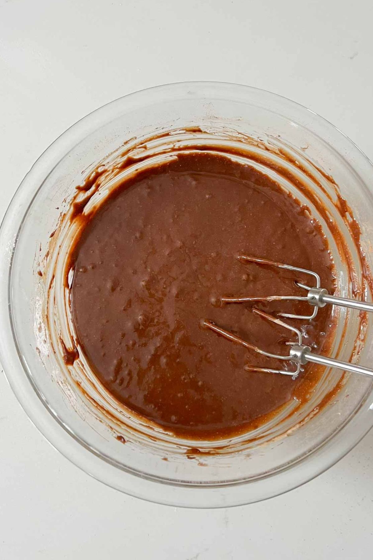 Oat flour brownie wet ingredients mixed together in a glass mixing bowl with silver beaters in the bowl.