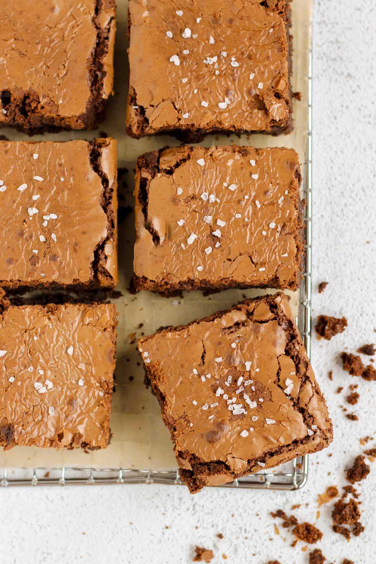 Oat flour brownies sprinkled with sea salt on a parchment paper lined wire cooling rack.