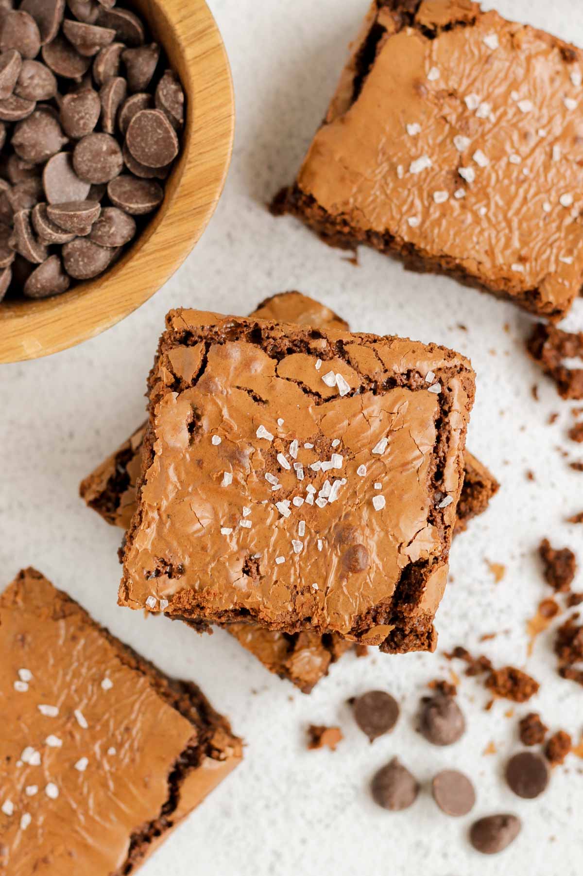 Oat flour brownies sprinkled with sea salt, with crumbs, and a bowl of chocolate chips on the side.