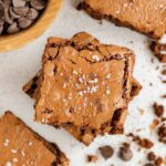 Oat flour brownies sprinkled with sea salt, with crumbs, and a bowl of chocolate chips on the side.