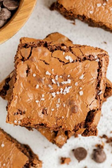 Oat flour brownies sprinkled with sea salt, with crumbs, and a bowl of chocolate chips on the side.