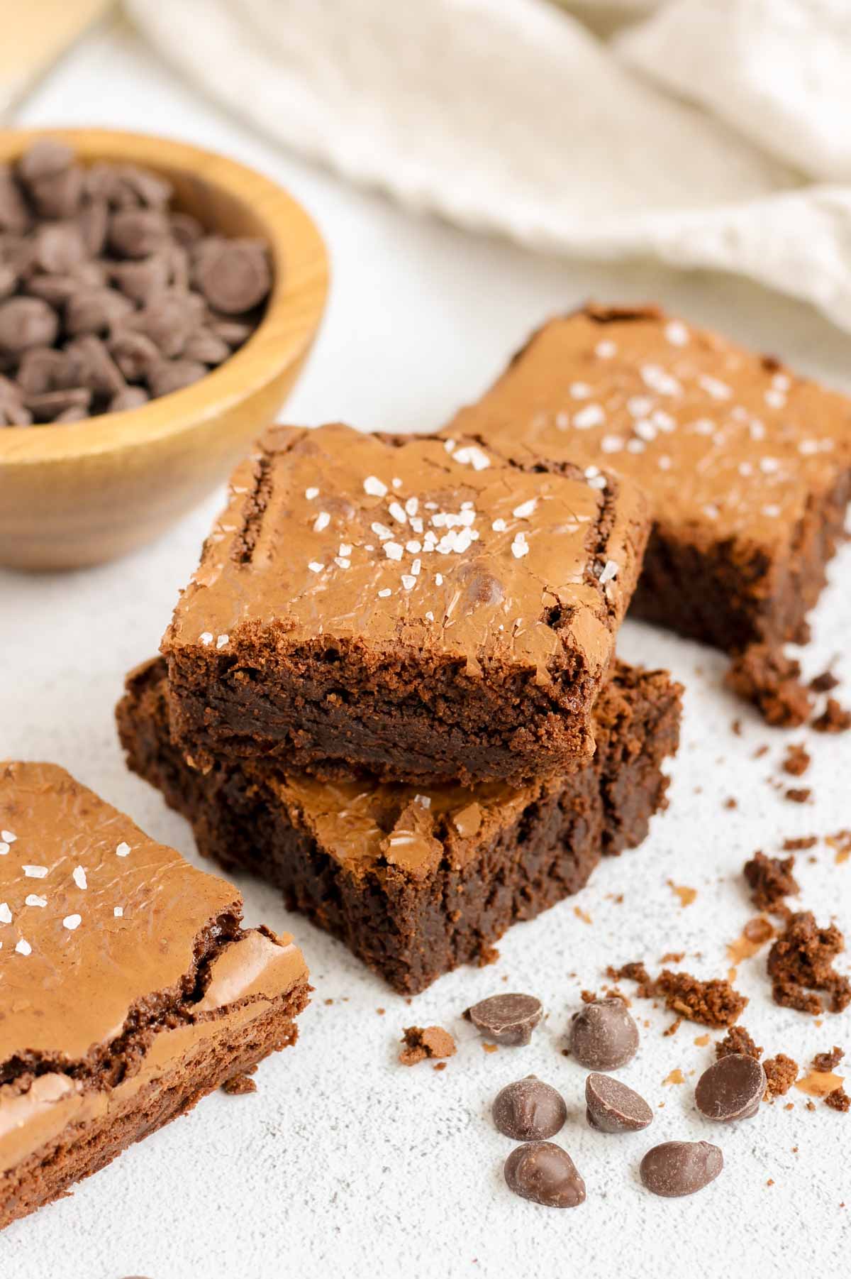 Oat flour brownies stacked 2 high with chocolate chips and crumbs sprinkled on the sides.