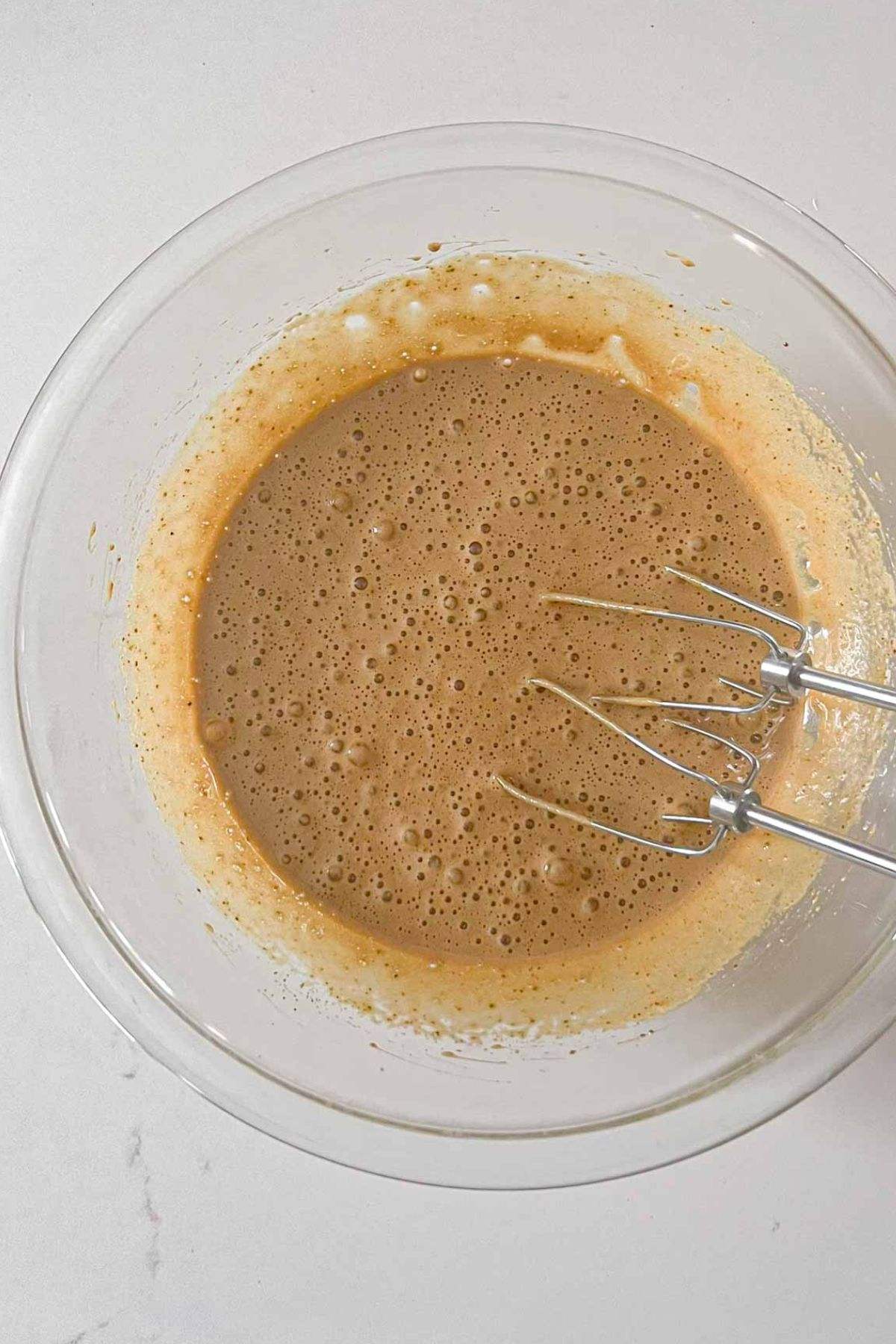 Eggs and coconut sugar are beaten together in a glass mixing bowl.