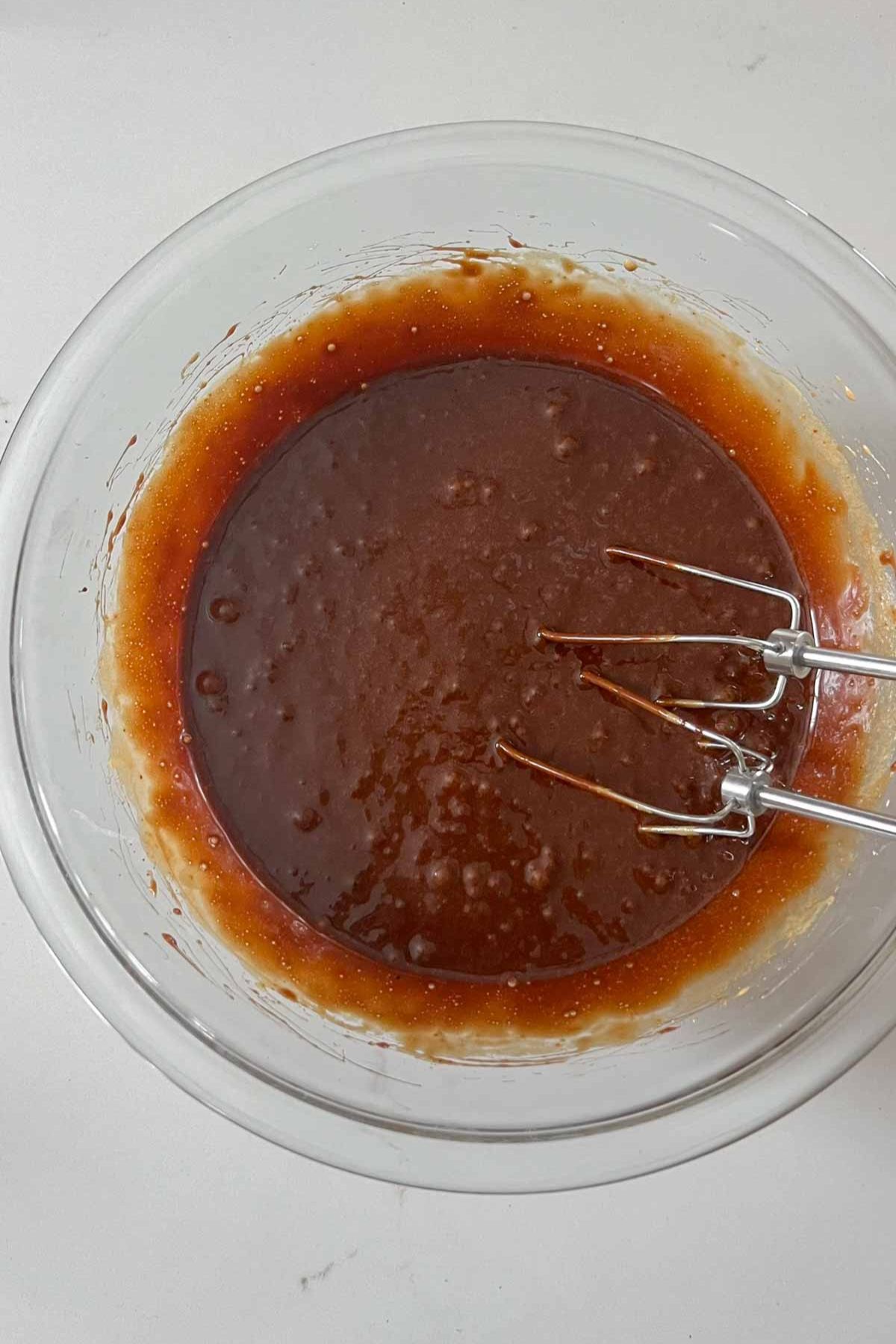 Chocolate brownie batter wet ingredients mixed together in a glass mixing bowl with silver beaters in the bowl.