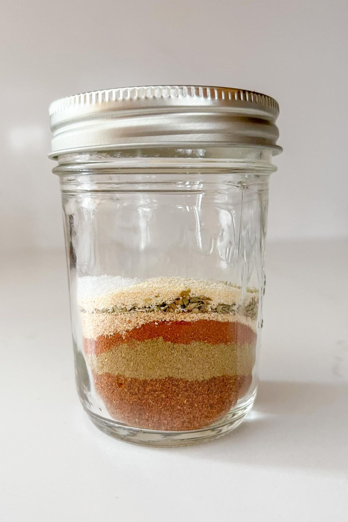Single spices needed for clean eating taco seasoning layered in a mason jar before being mixed.