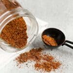 Taco seasoning spilling from a mason jar with a tablespoon on the side filled with taco seasoning.