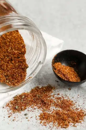 Taco seasoning spilling from a mason jar with a tablespoon on the side filled with taco seasoning.