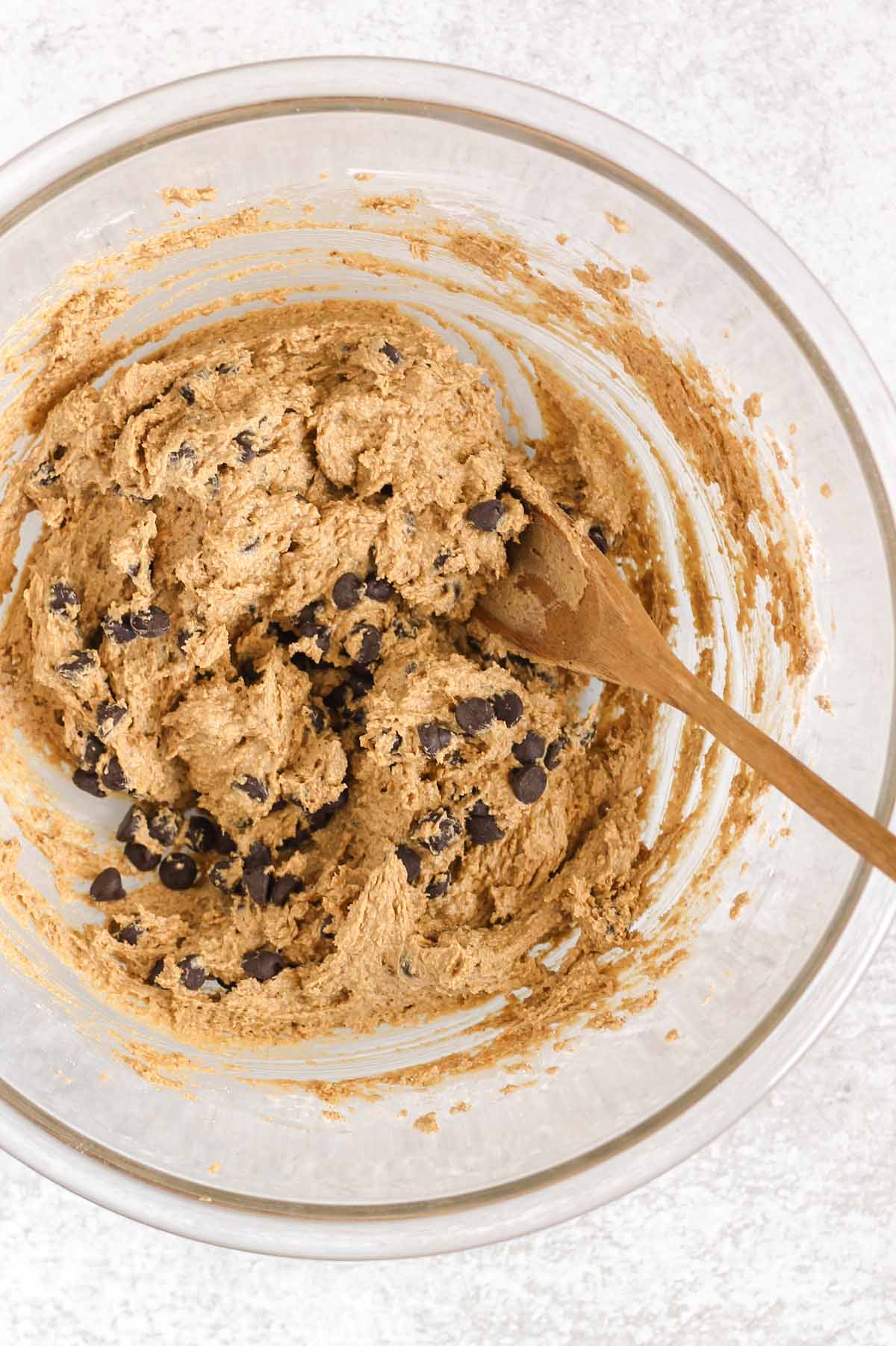 Chocolate chips folded into cookie dough with a wooden spoon.