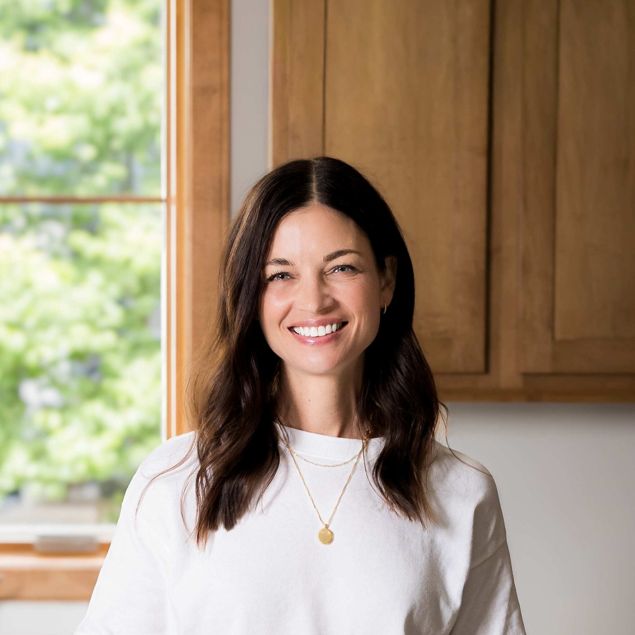 Woman with shoulder length brown hair standing in a kitchen.