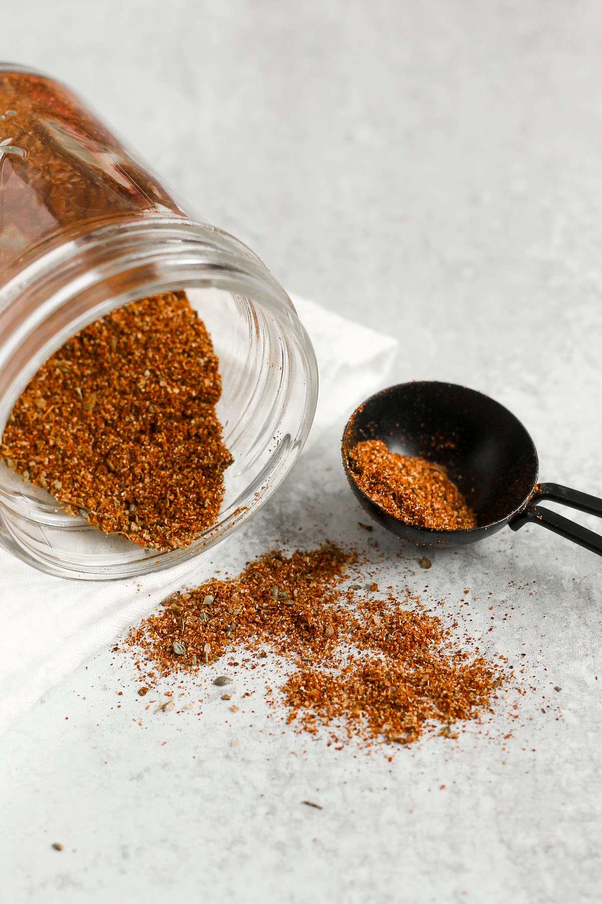 Taco seasoning spilling from a mason jar with a tablespoon on the side filled with taco seasoning.