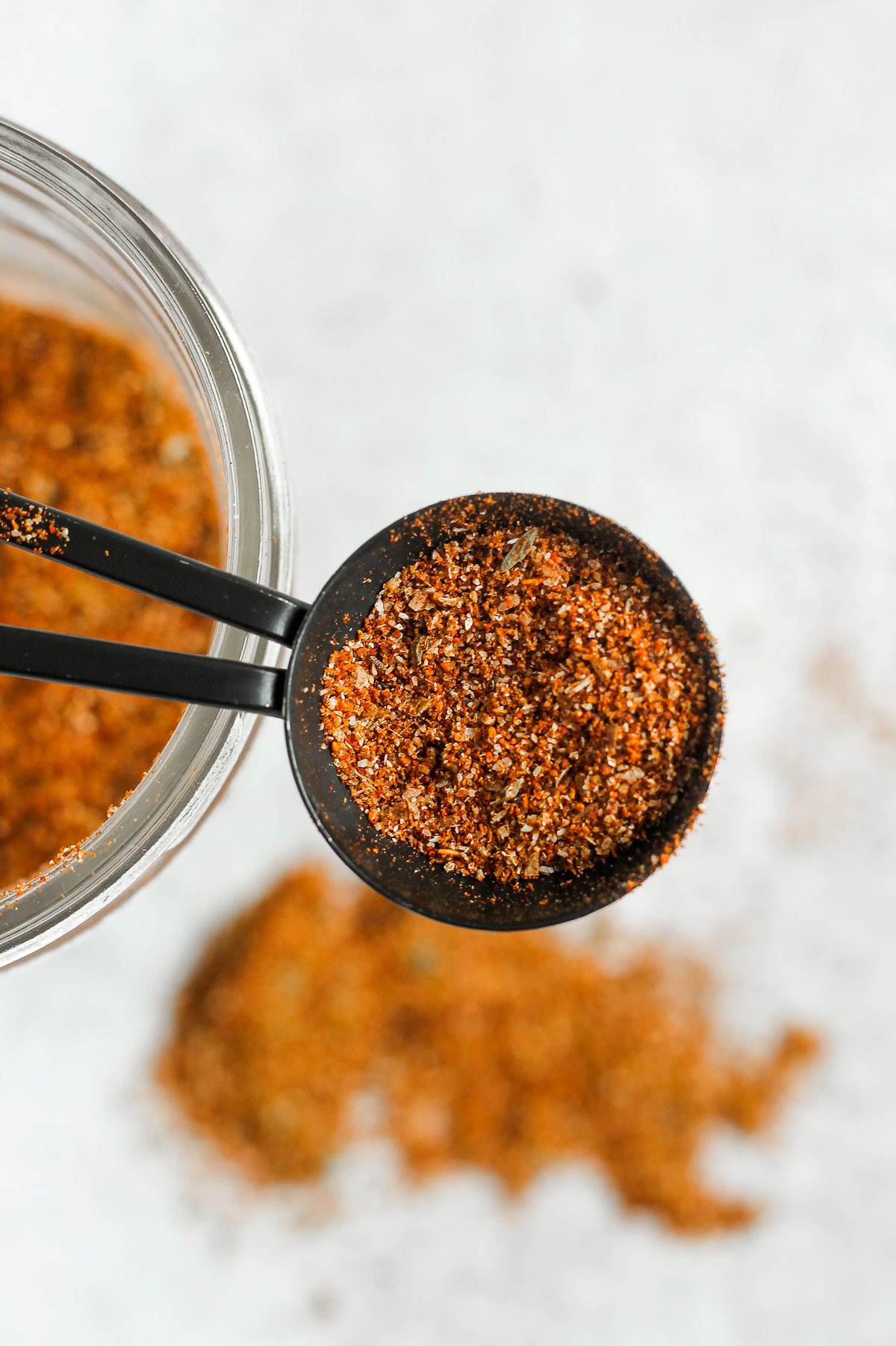 Measuring tablespoon filled with taco seasoning with a mason jar of taco seasoning in the background.