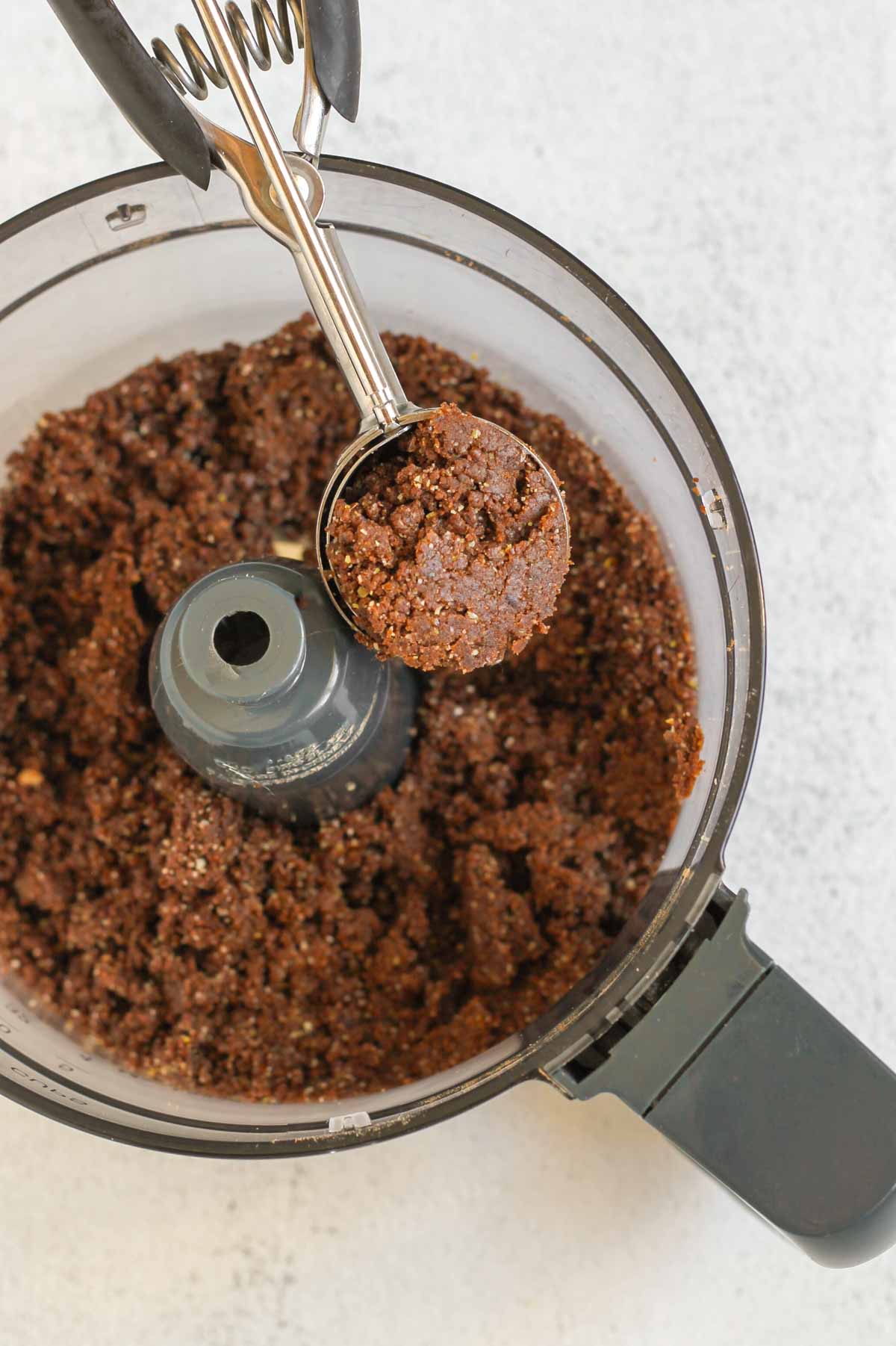 Spring loaded scoop scooping out protein brownie dough from a food processor.