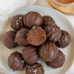 Chocolate brownie bites stacked on a small plate with a bit taken from the top ball.