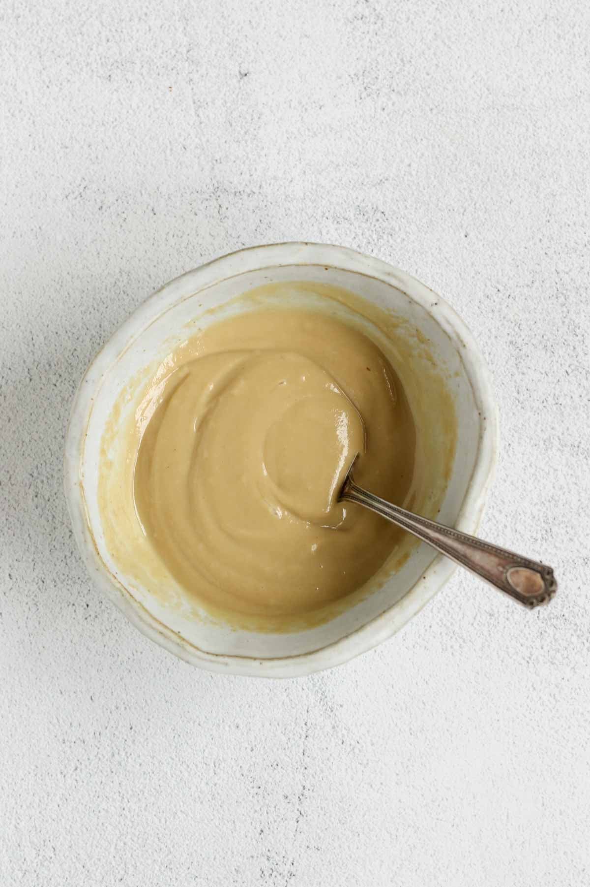 Maple tahini dressing mixed in a shallow bowl with a fork in the bowl.