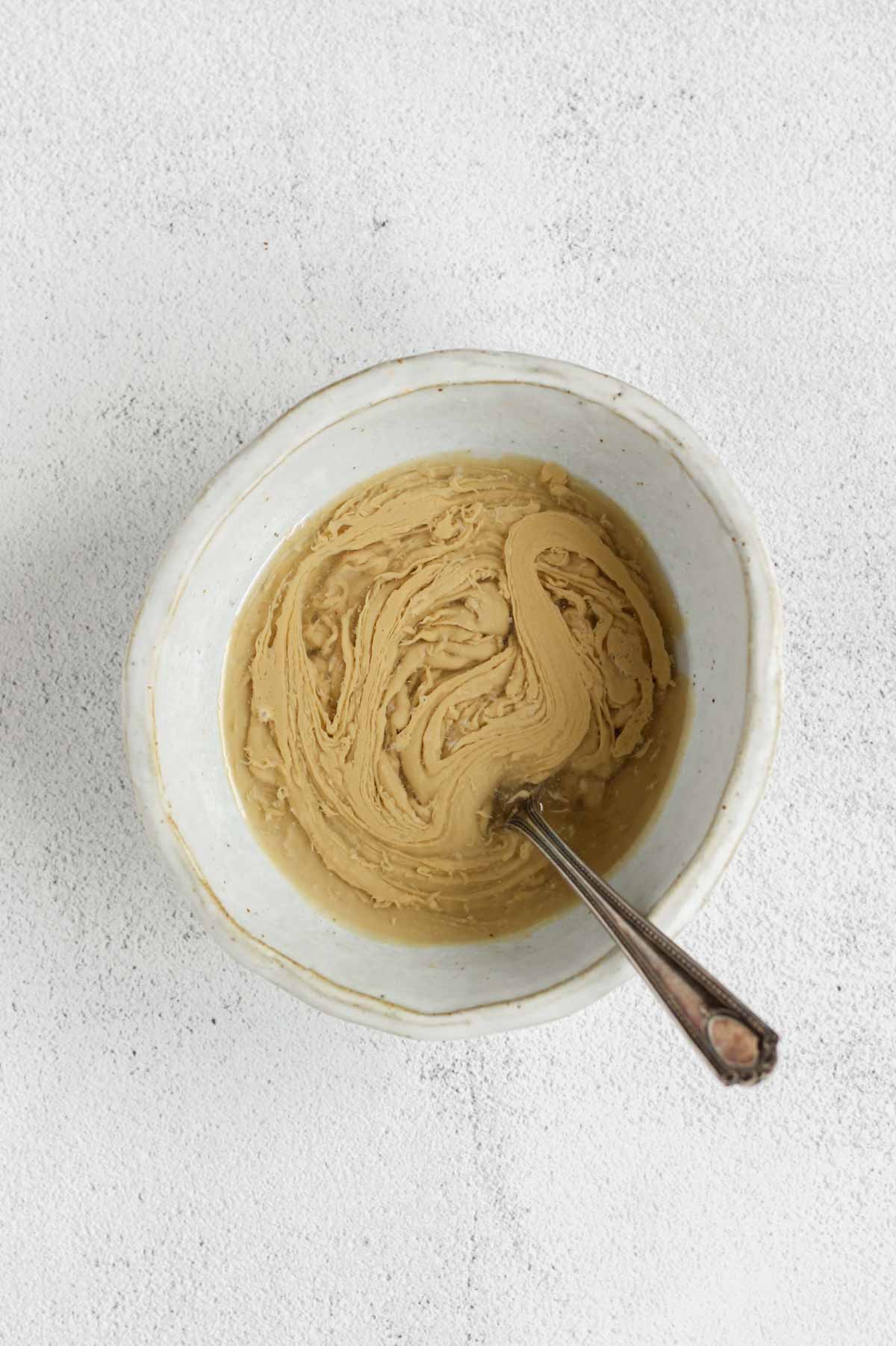 Maple tahini dressing ingredients being mixed in a shallow bowl.