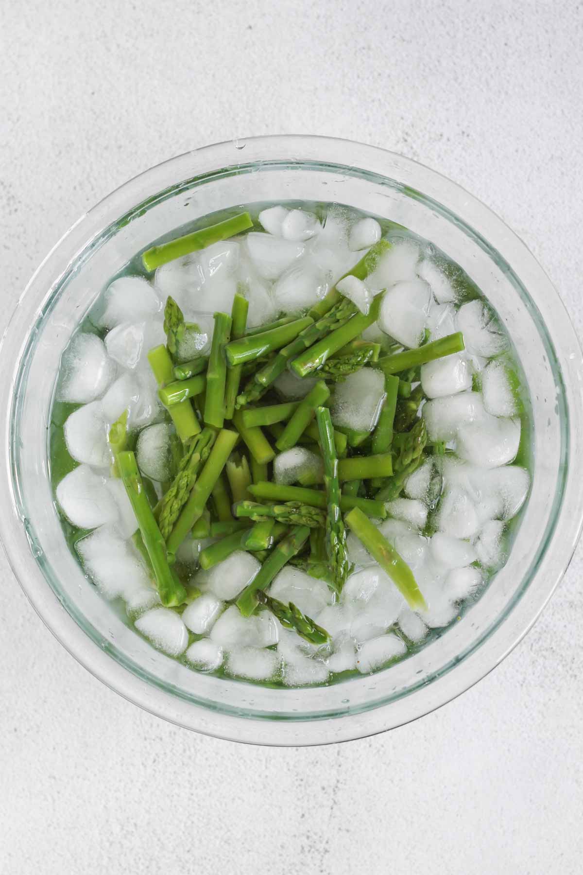 Chopped asparagus in a small bowl with water and ice.