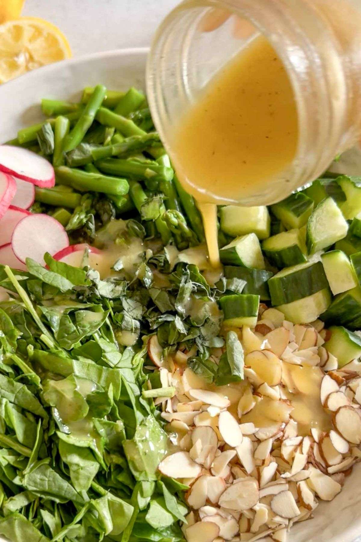 Lemon dressing being poured from a mason jar over asparagus and quinoa salad.
