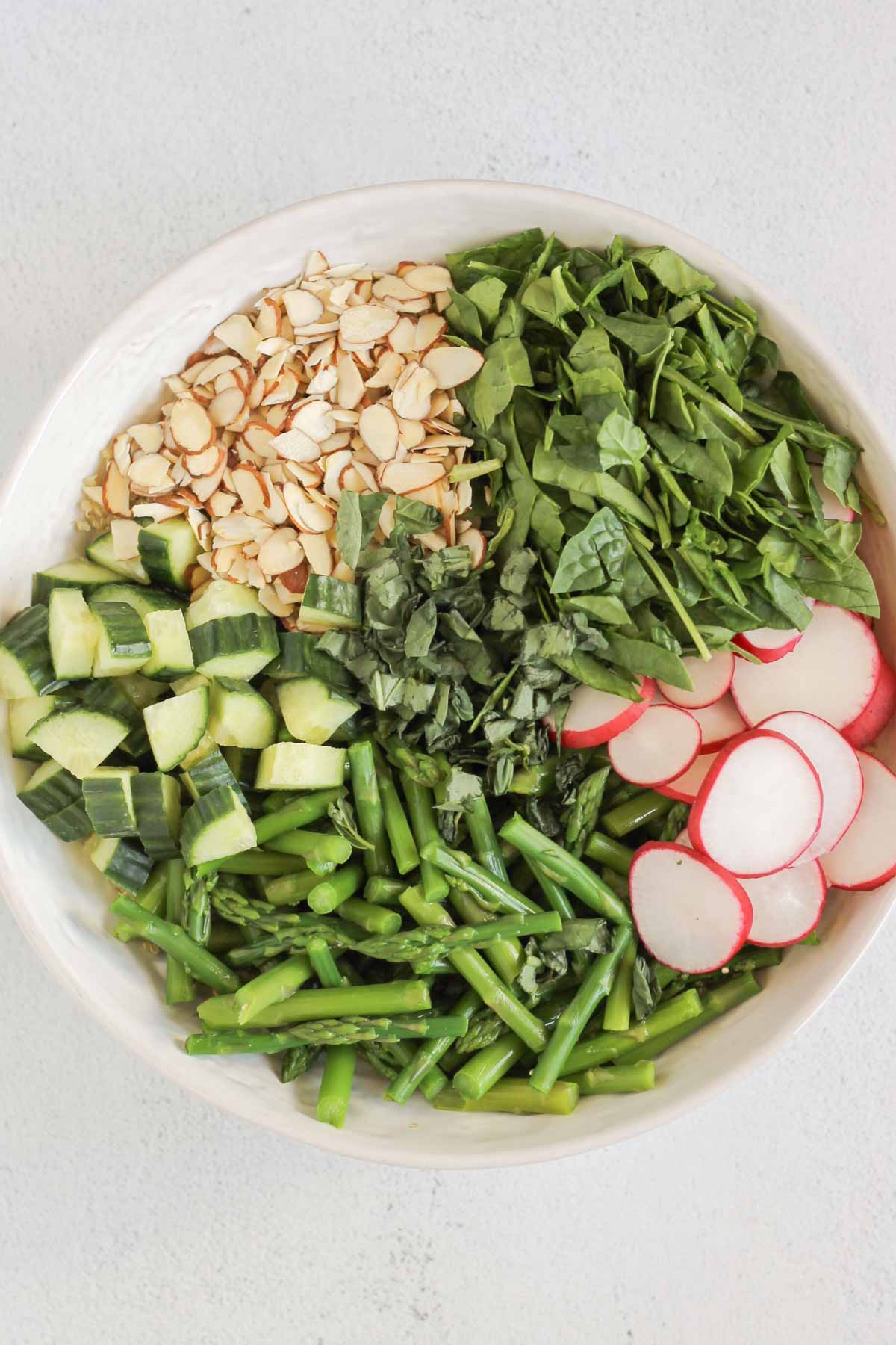 Ingredients for asparagus quinoa salad in individual sections in a large serving bowl.