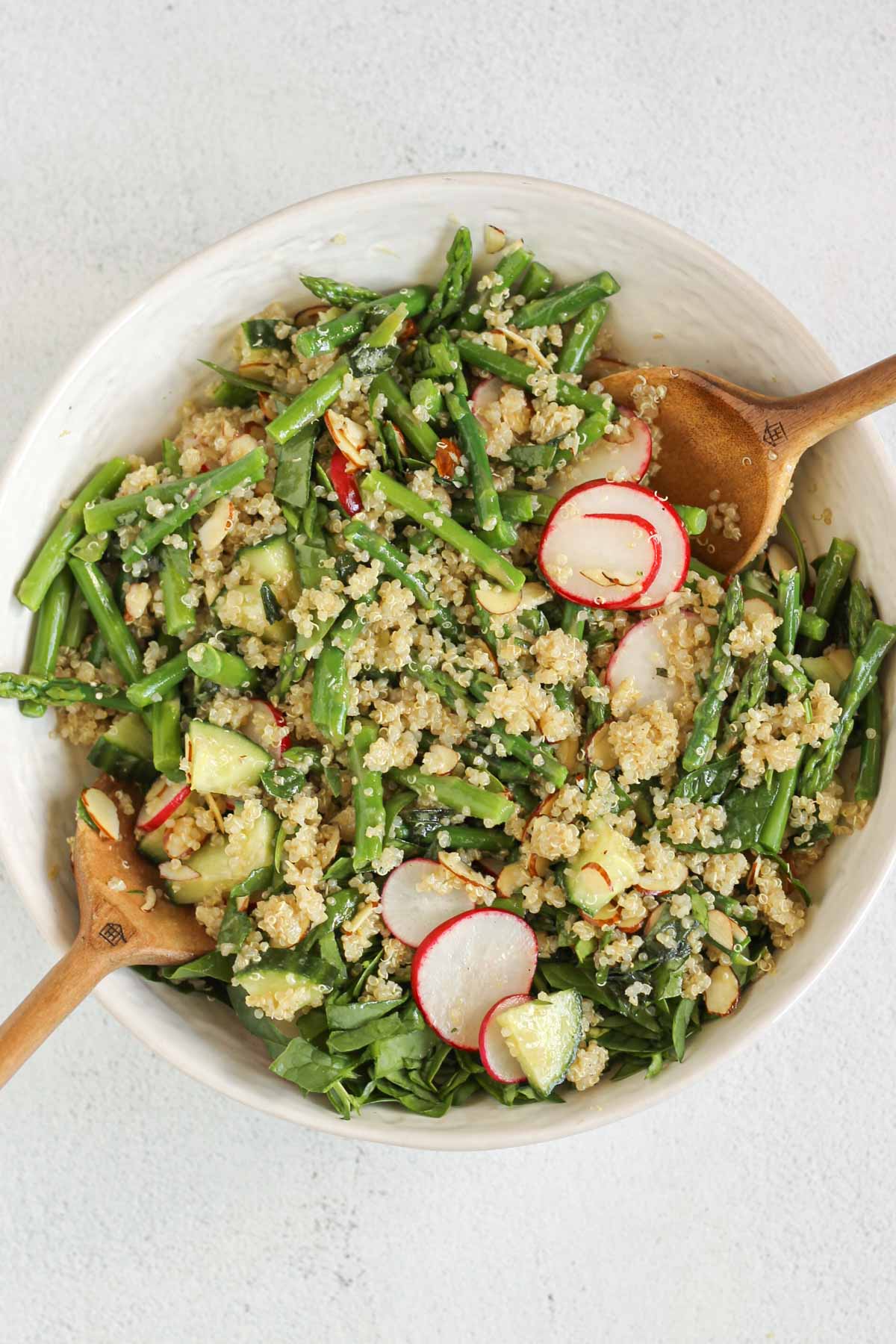 Two wooden salad utensils mixing quinoa and asparagus salad in a large ceramic bowl.