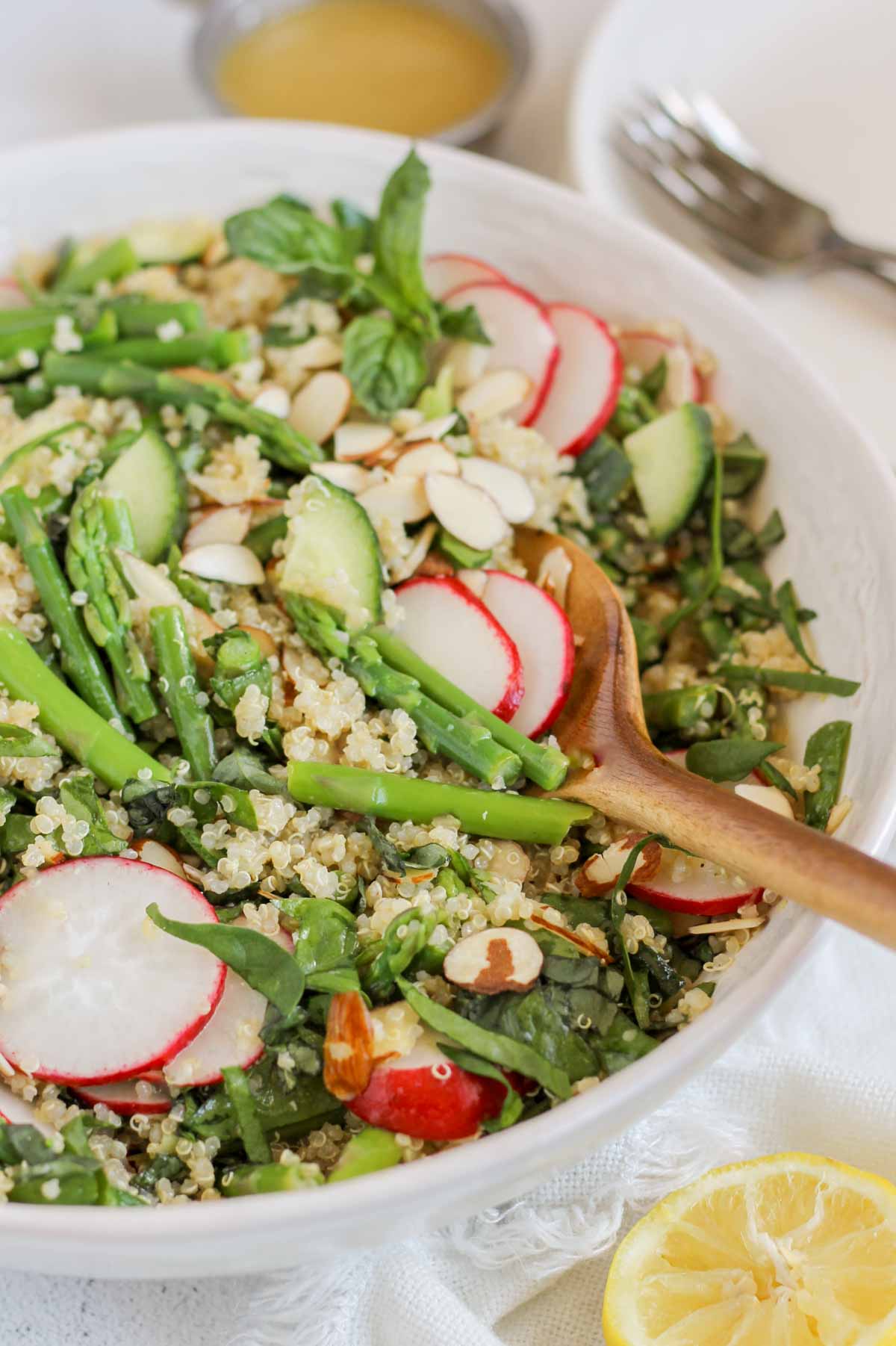 Asparagus and quinoa salad in a large serving bowl with a large wooden spoon scooping out some salad.