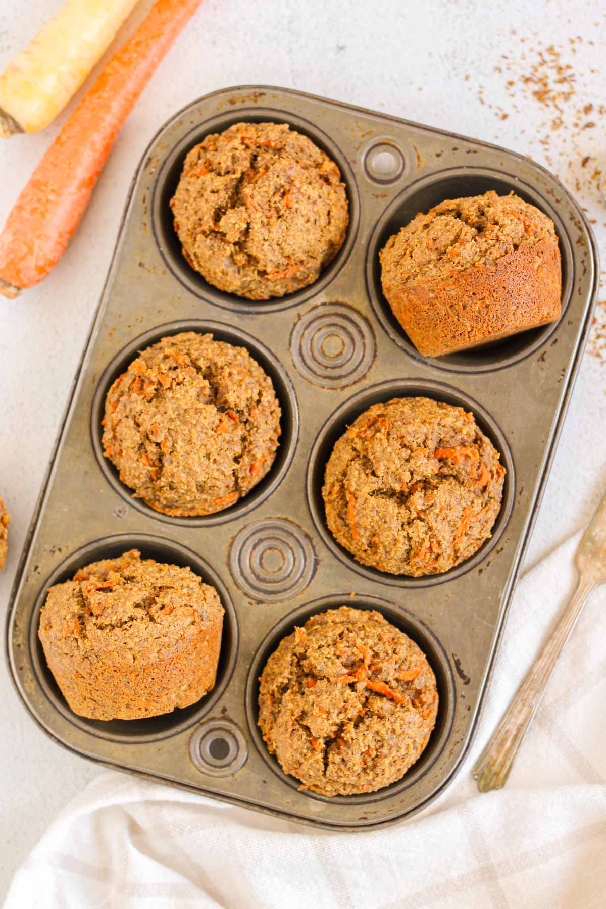 Carrot flaxseed muffins in a 6-cup vintage muffin tin with carrots on the side.