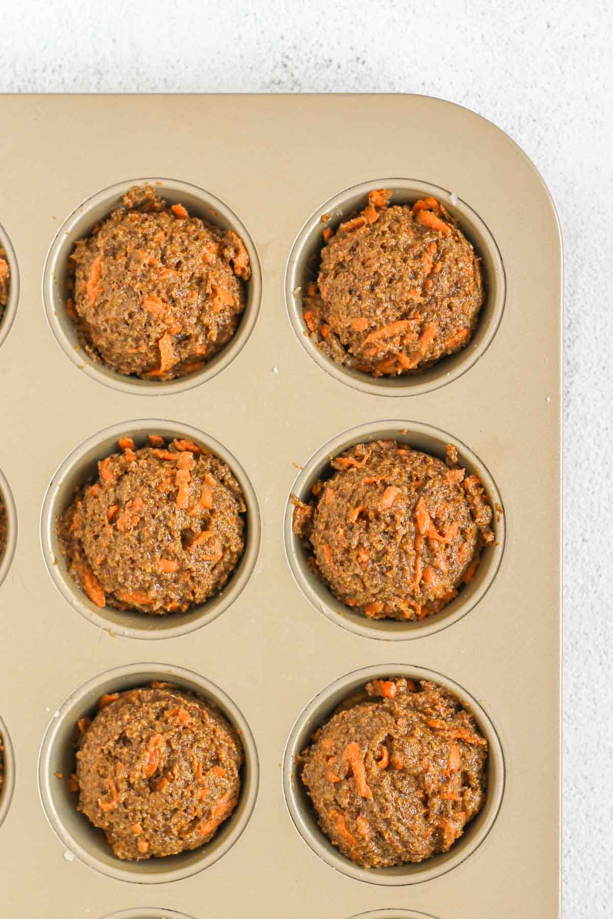 Carrot flaxseed muffin batter scooped into a muffin tin.