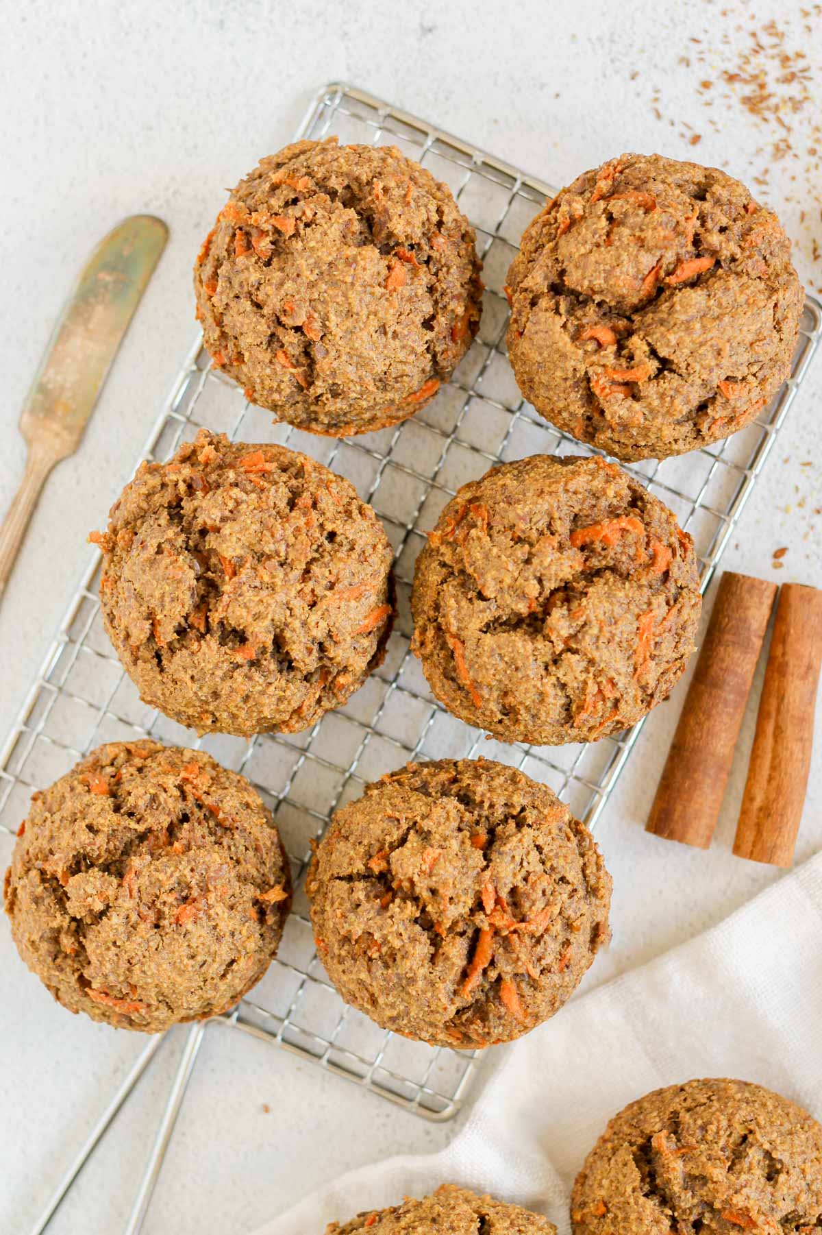Six carrot flaxseed muffins on a rectangular wire cooling rack with a vintage butter knife on the side.