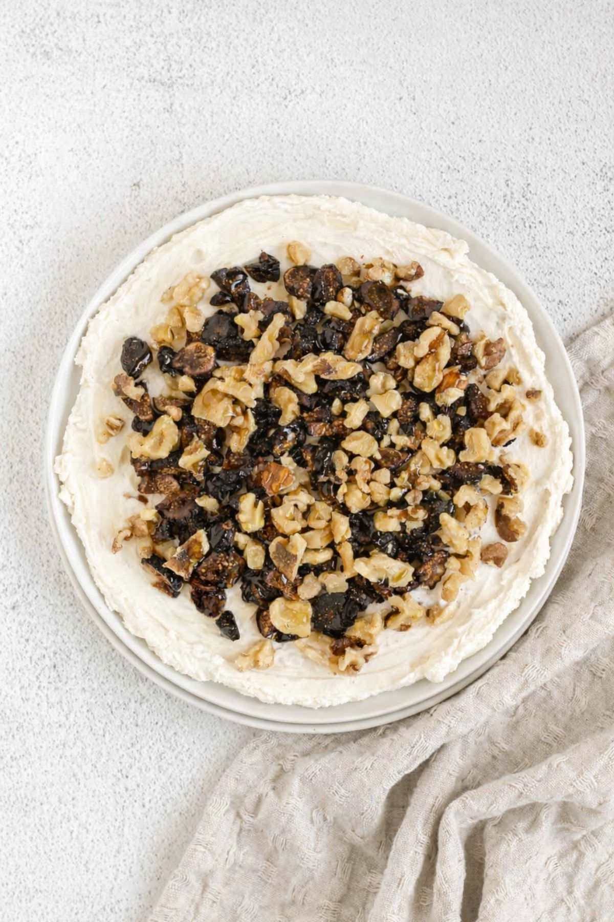 Goat cheese spread on a round plate topped with sliced figs and chopped walnuts.