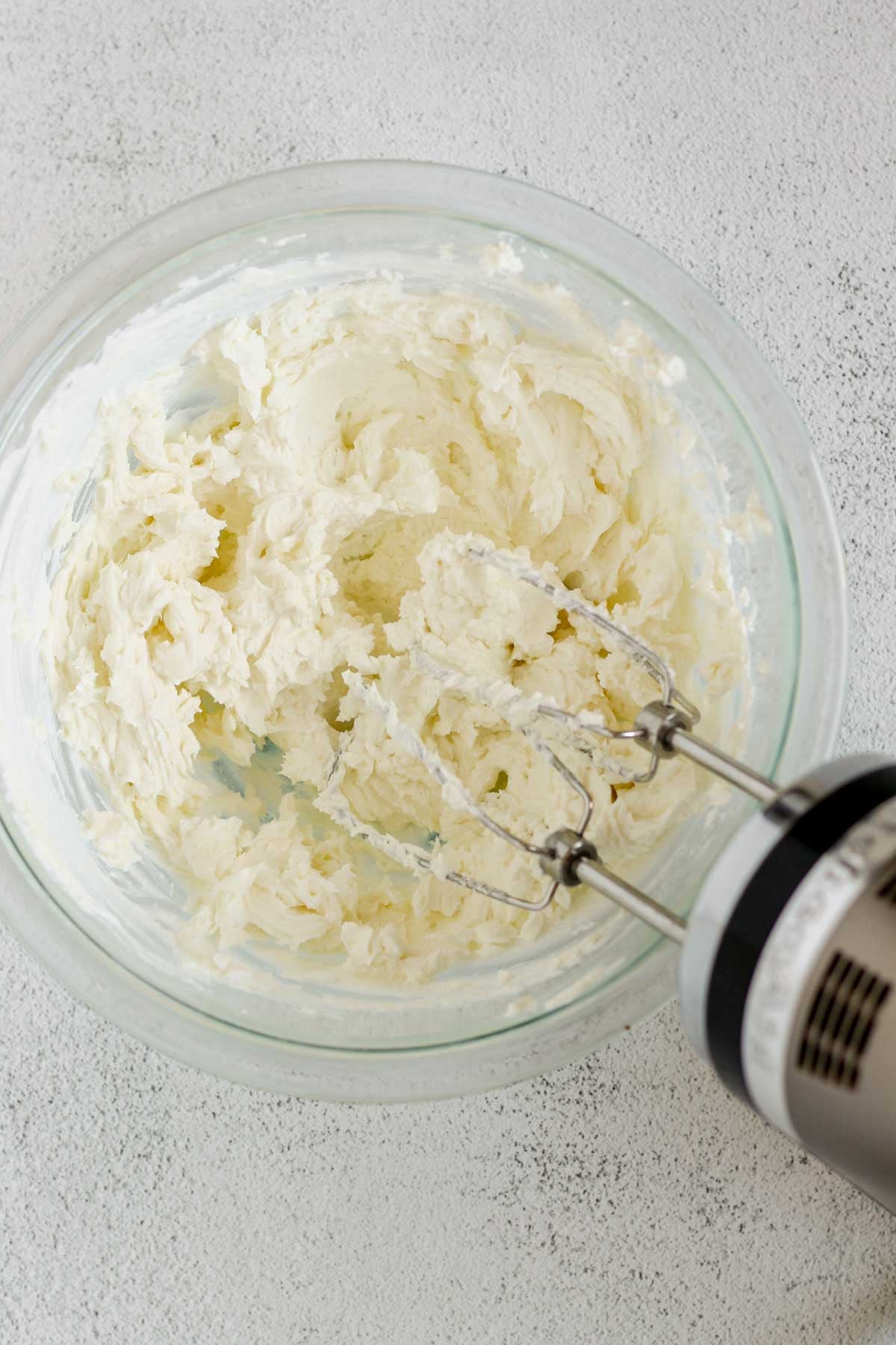 Goat cheese and yogurt whipped in a glass mixing bowl with a hand-held mixer in the bowl.