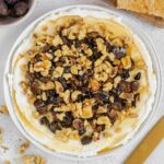 Whipped goat cheese topped with honey, sliced dried figs and walnuts on a small round plate.
