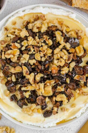 Whipped goat cheese topped with honey, sliced dried figs and walnuts on a small round plate.