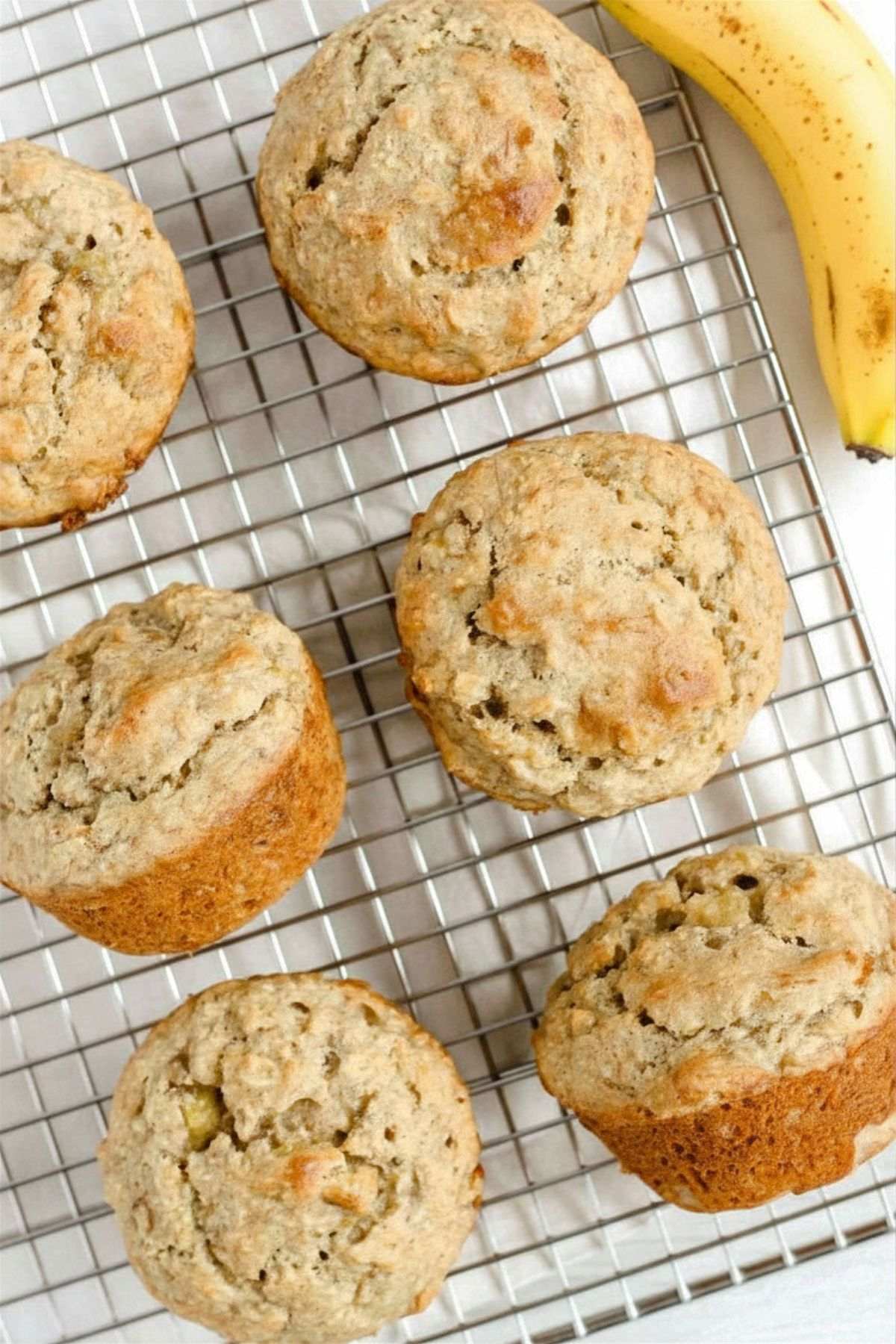 Banana oat muffins on a wire cooling rack with a banana on the side.