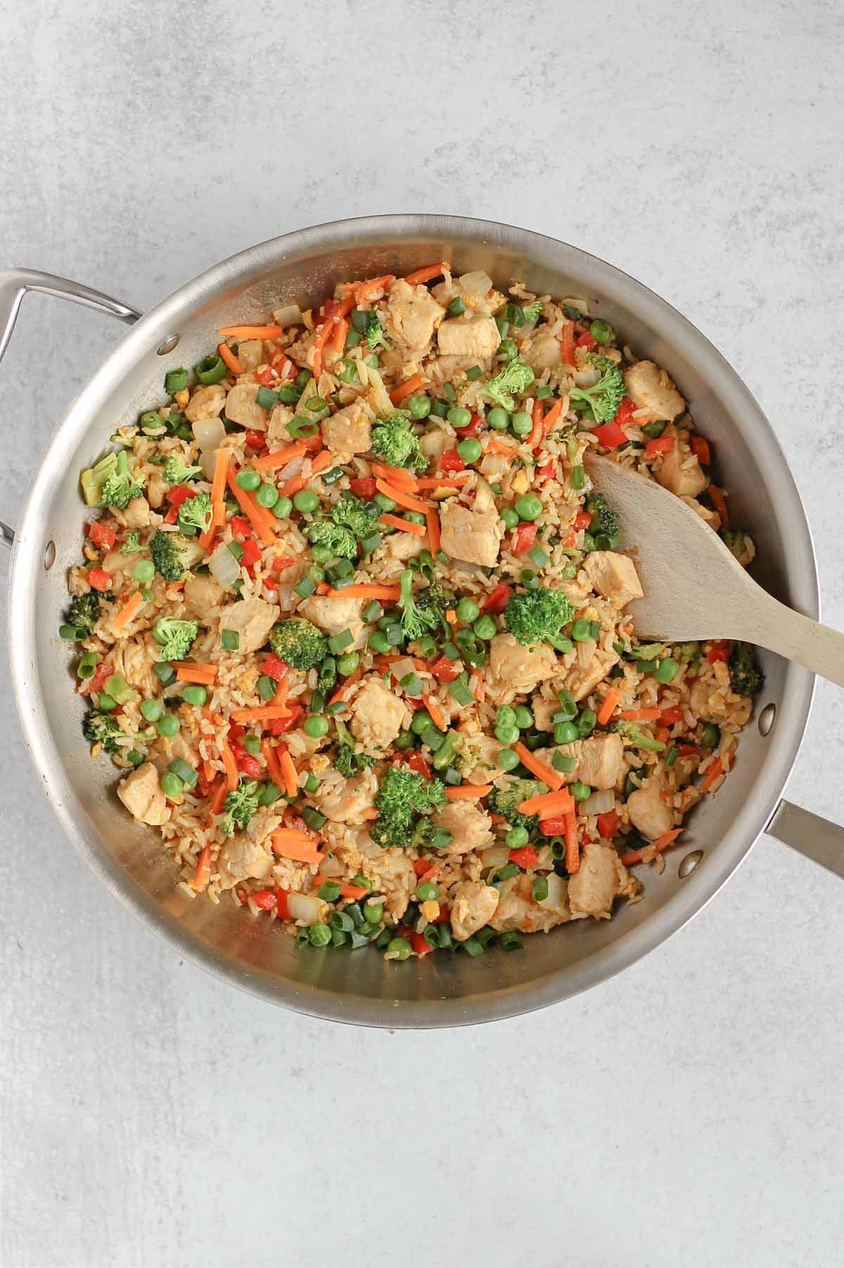 Chicken fried rice in a large cast iron skillet with a wooden spatula in the fried rice.