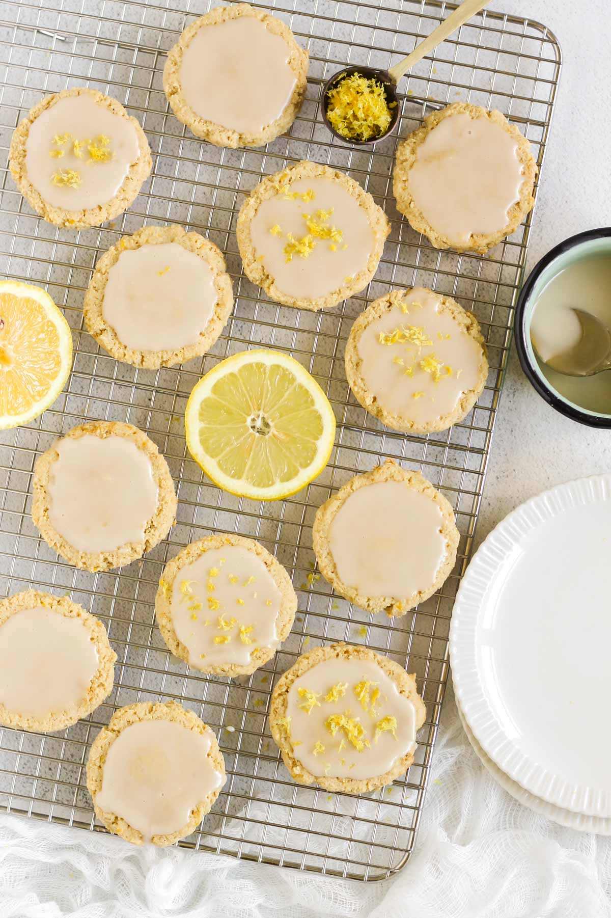 Almond flour lemon cookies topped with a glaze on a rectangular wire cooling rack with slices of lemon placed on the rack.