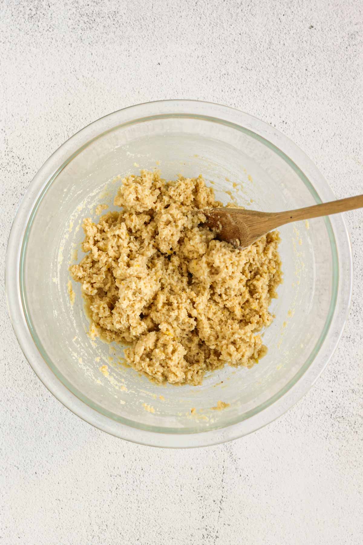 Almond flour lemon cookie dough mixed in a glass mixing bowl with a wooden spoon in the bowl.