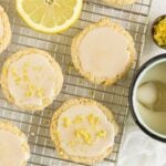 Almond flour lemon cookies topped with a glaze on a rectangular wire cooling rack with slices of lemon placed on the rack.