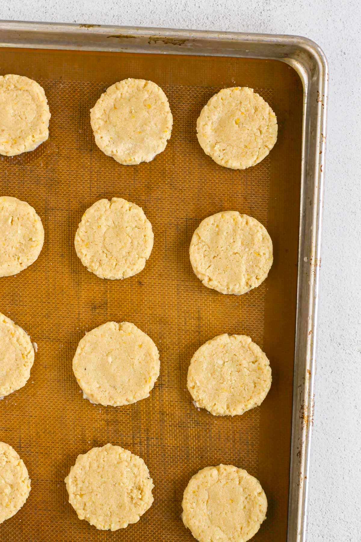 Almond flour cookie dough shaped into round cookies on a silicone mat lined baking sheet before being baked.