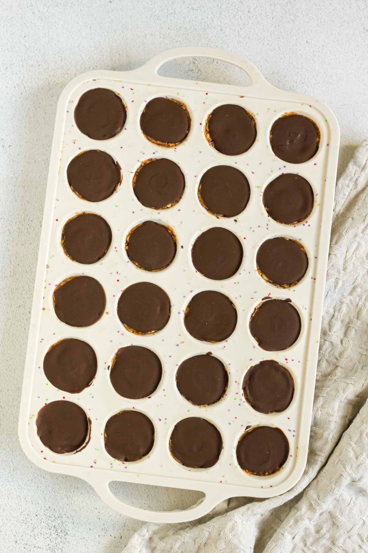 24-cup silicone muffin pan filled with peanut butter brown rice bites topped with chocolate that has set.