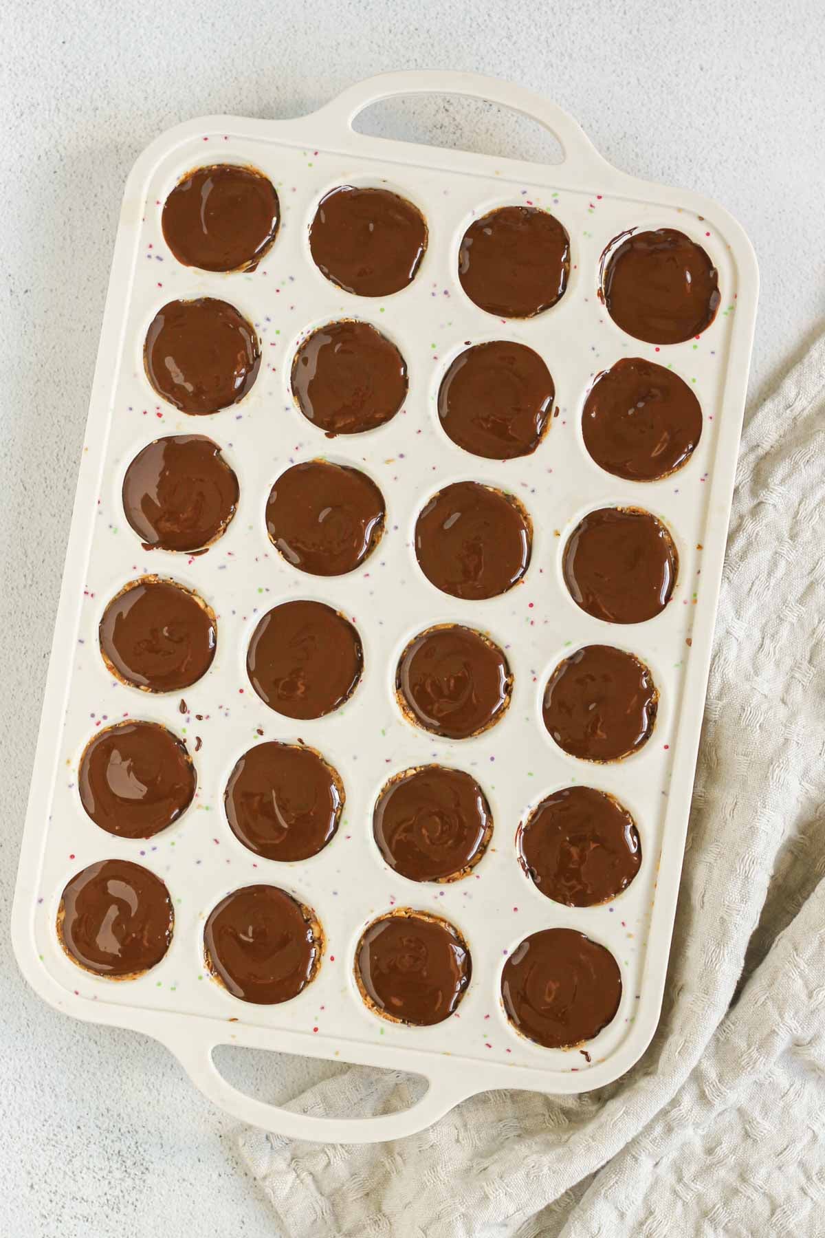 24-cup silicone muffin pan filled with peanut butter brown rice bites topped with melted chocolate.