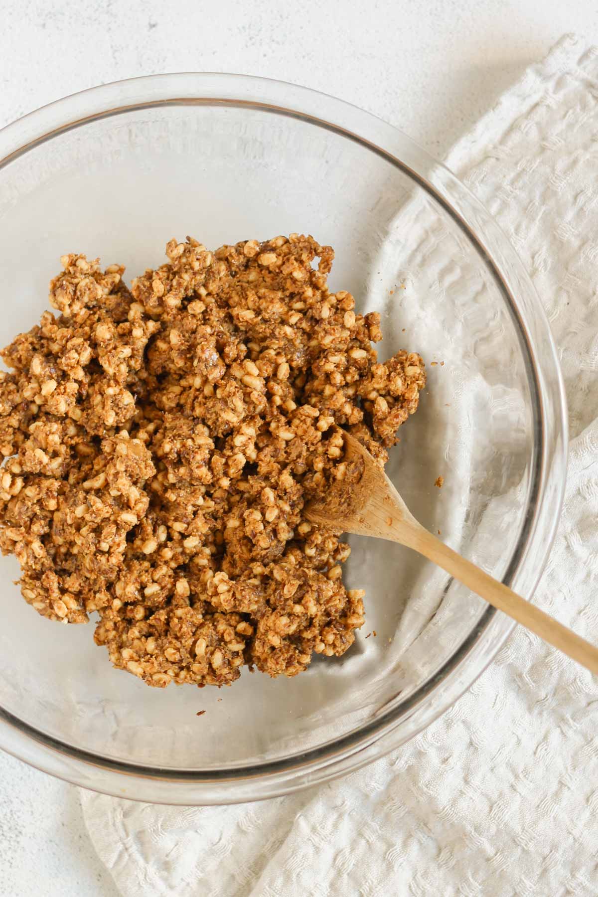 Peanut butter and honey combined with brown rice crisps and flaxseeds in a large glass mixing bowl.