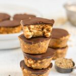 Peanut butter crispy bites stacked 4 high with a bite taken from the top one and additional crispy bites in the background.
