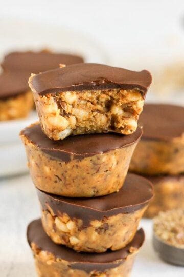 Peanut butter crispy bites stacked 4 high with a bite taken from the top one and additional crispy bites in the background.