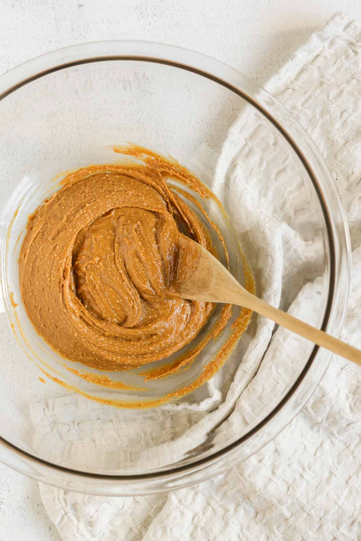 Peanut butter and honey mixed together in a large glass mixing bowl with a wooden spoon in the bowl.